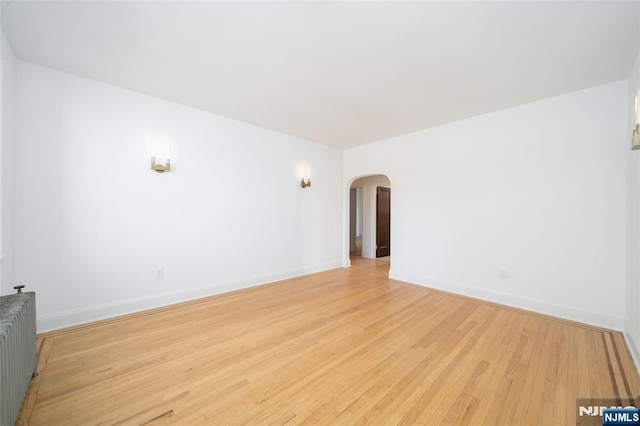 1100 83rd St Unit 301, North Bergen, NJ 07047 - empty room featuring radiator heating unit, arched walkways, and light wood-style floors