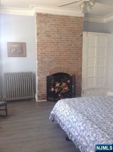 17 48th St, Weehawken, NJ 07086 - bedroom with radiator heating unit, wood finished floors, crown molding, a fireplace, and ceiling fan