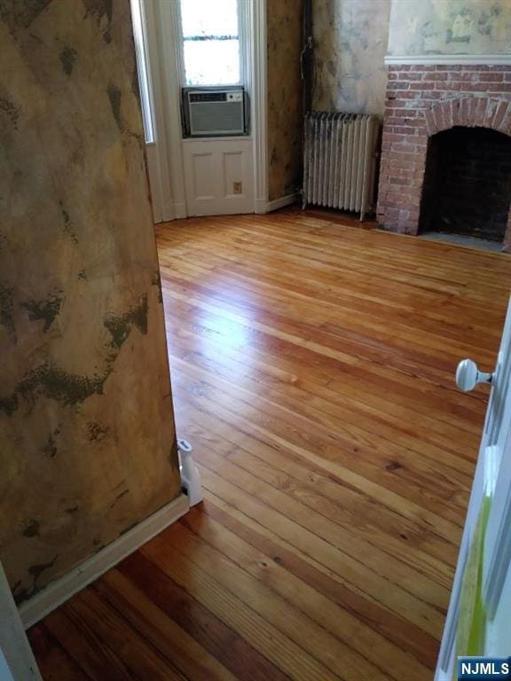 17 48th St, Weehawken, NJ 07086 - unfurnished living room with radiator heating unit, light wood-type flooring, cooling unit, and a fireplace