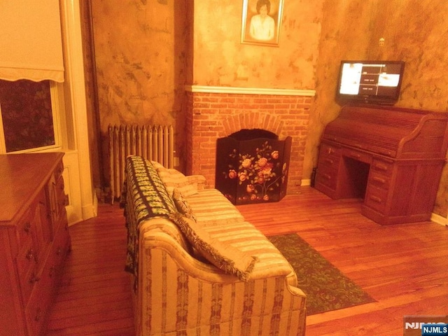 17 48th St, Weehawken, NJ 07086 - living room featuring radiator, wood finished floors, wallpapered walls, and a brick fireplace