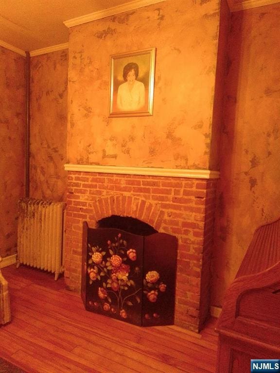 17 48th St, Weehawken, NJ 07086 - detailed view of radiator, wood finished floors, ornamental molding, a brick fireplace, and wallpapered walls