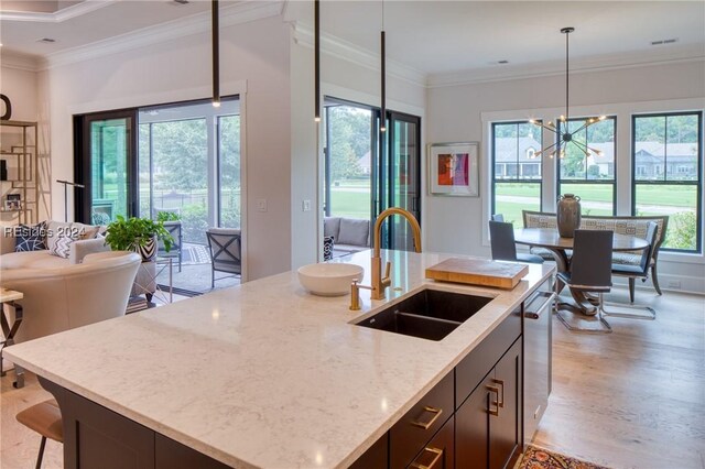 kitchen with sink, crown molding, a kitchen island with sink, light stone countertops, and decorative light fixtures