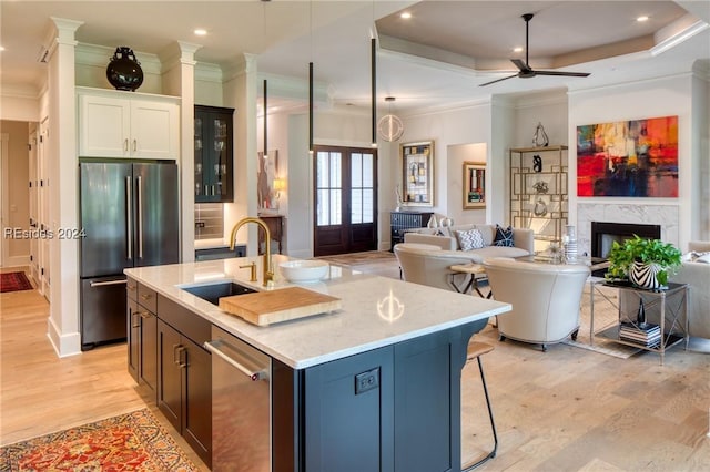 kitchen featuring sink, appliances with stainless steel finishes, white cabinetry, a tray ceiling, and a center island with sink