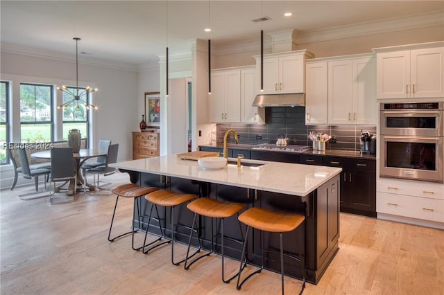 kitchen featuring sink, hanging light fixtures, stainless steel appliances, white cabinets, and a center island with sink