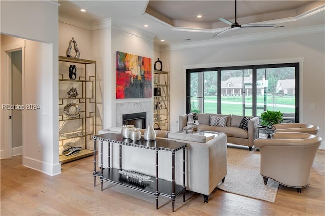 living room with ornamental molding, a tray ceiling, a high end fireplace, and light hardwood / wood-style flooring