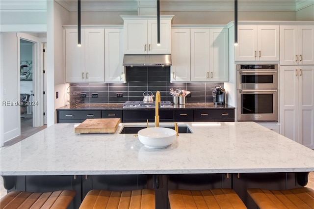 kitchen with double oven, an island with sink, white cabinets, and a kitchen bar