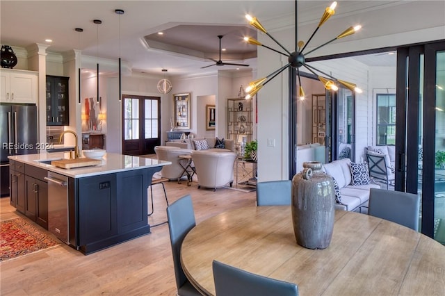 dining room with crown molding, sink, a tray ceiling, and light wood-type flooring