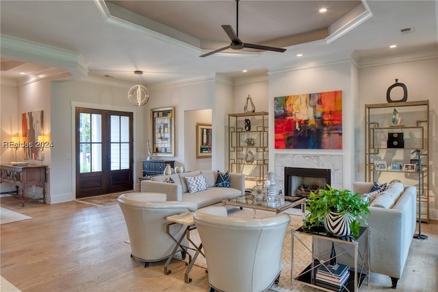 living room featuring crown molding, a premium fireplace, a raised ceiling, and light hardwood / wood-style floors