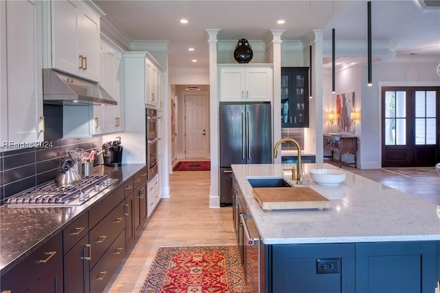 kitchen featuring stainless steel appliances, tasteful backsplash, ornamental molding, white cabinets, and a center island with sink