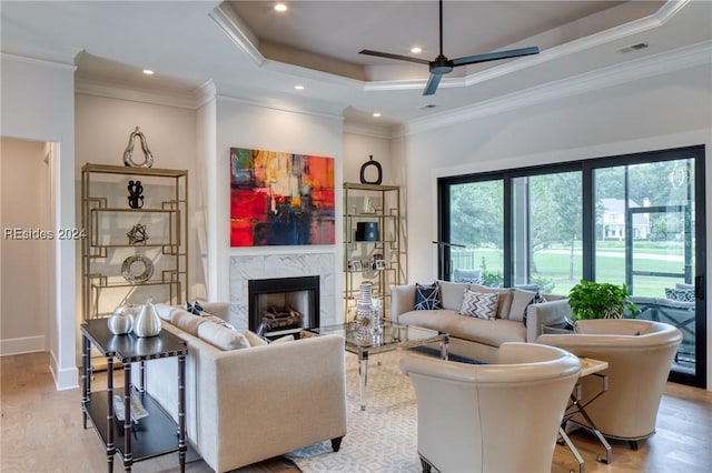 living room with crown molding, a raised ceiling, ceiling fan, a fireplace, and light hardwood / wood-style floors