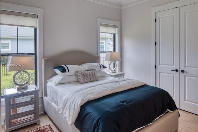 bedroom featuring crown molding, a closet, light hardwood / wood-style floors, and multiple windows