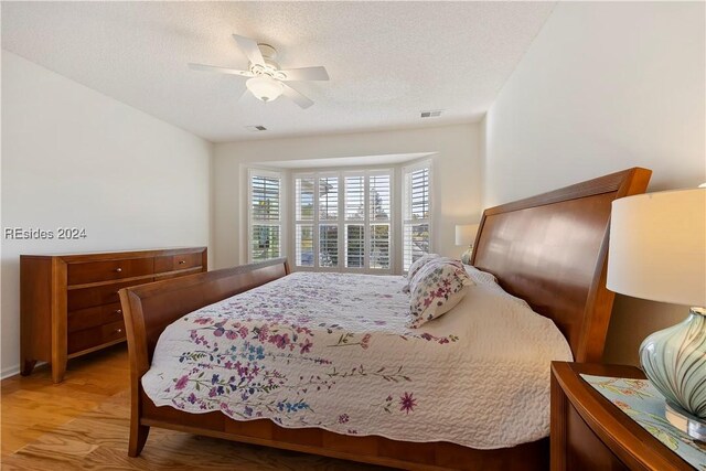 bedroom with a textured ceiling, ceiling fan, and light hardwood / wood-style flooring