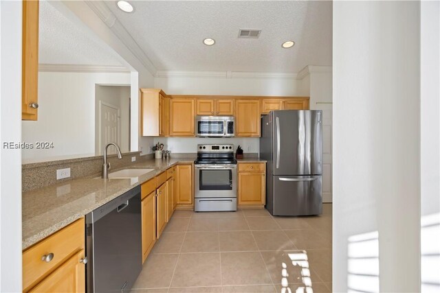 kitchen with sink, light tile patterned floors, stainless steel appliances, ornamental molding, and light stone countertops