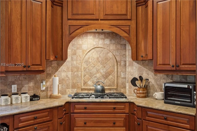 kitchen featuring light stone counters, backsplash, and stainless steel gas cooktop