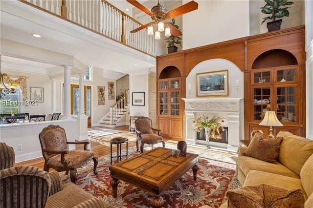 living room featuring a high ceiling, ceiling fan with notable chandelier, hardwood / wood-style floors, and ornate columns