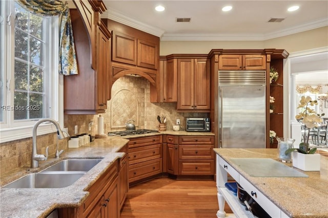 kitchen featuring appliances with stainless steel finishes, sink, backsplash, ornamental molding, and light wood-type flooring