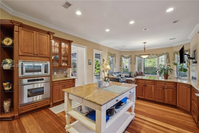 kitchen featuring appliances with stainless steel finishes, hanging light fixtures, light stone counters, ornamental molding, and light hardwood / wood-style floors