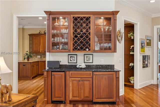 bar featuring dark stone countertops, ornamental molding, decorative backsplash, and light wood-type flooring