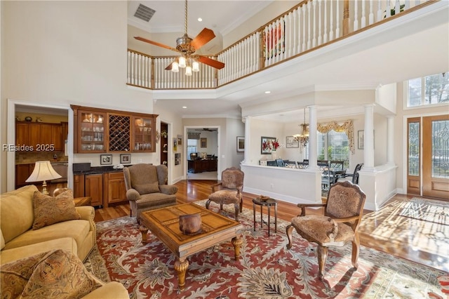 living room featuring ornamental molding, decorative columns, light hardwood / wood-style flooring, and a high ceiling