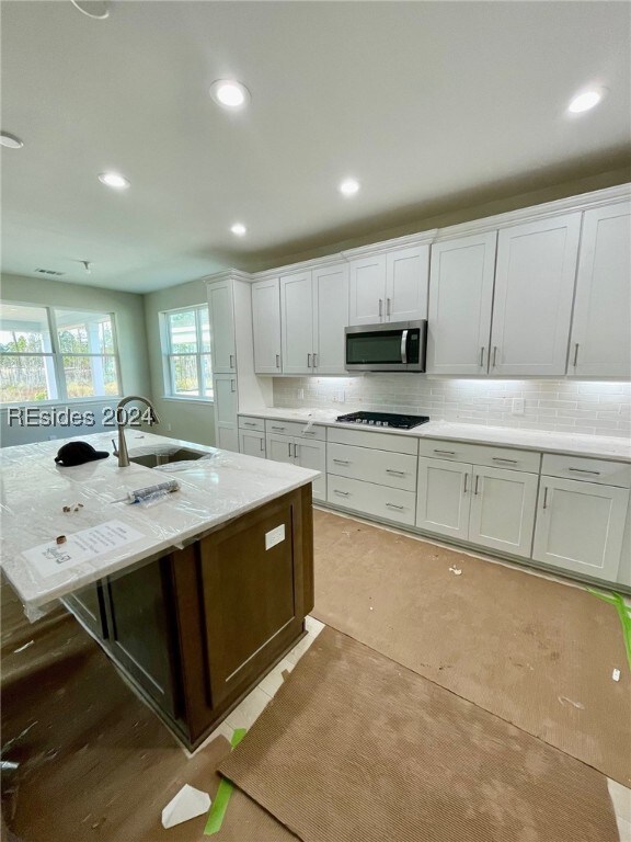 kitchen featuring white cabinetry, sink, a kitchen island with sink, light stone counters, and black gas stovetop