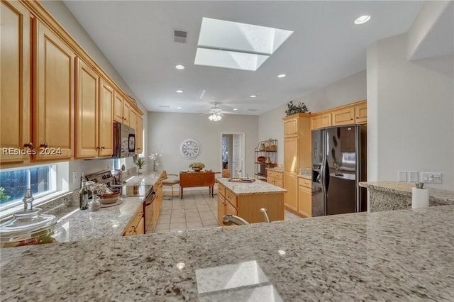 kitchen with a skylight, a center island, light tile patterned floors, black fridge with ice dispenser, and light stone countertops