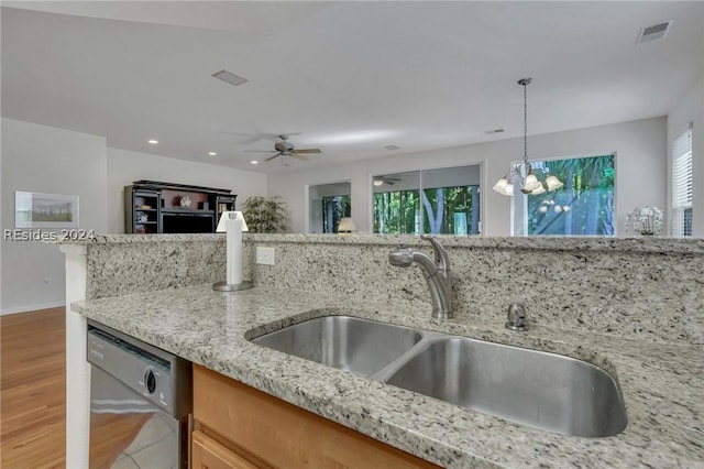 kitchen with sink, hanging light fixtures, dishwasher, light stone countertops, and ceiling fan with notable chandelier