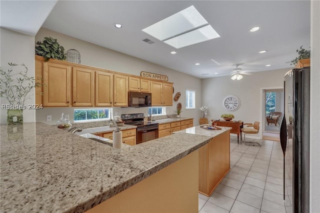 kitchen with light tile patterned floors, a skylight, light stone counters, black appliances, and kitchen peninsula