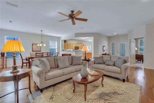 living room with ceiling fan with notable chandelier and light wood-type flooring