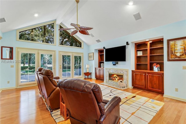 living room with ceiling fan, high vaulted ceiling, a fireplace, light hardwood / wood-style floors, and built in shelves