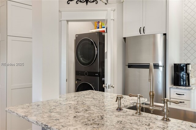 kitchen with white cabinetry, stacked washer and clothes dryer, and stainless steel refrigerator