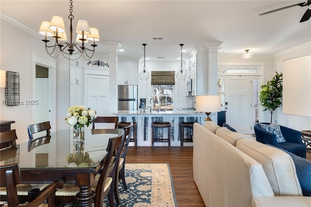 dining space with sink, crown molding, dark hardwood / wood-style flooring, ceiling fan with notable chandelier, and ornate columns