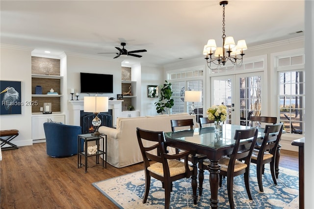 dining space featuring french doors, crown molding, built in features, hardwood / wood-style flooring, and ceiling fan with notable chandelier