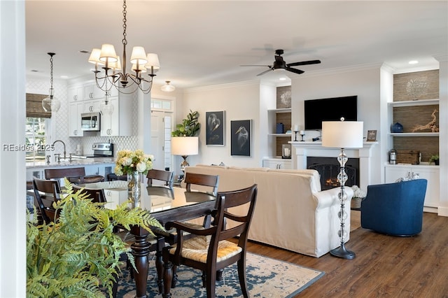 dining space with dark hardwood / wood-style flooring, sink, ceiling fan with notable chandelier, and ornamental molding