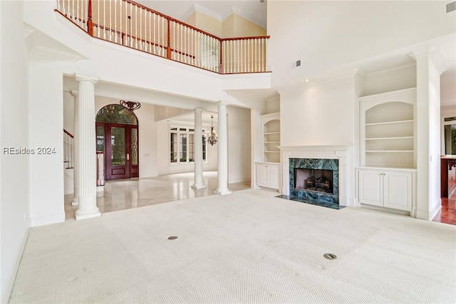 unfurnished living room with a fireplace, decorative columns, built in features, and a high ceiling