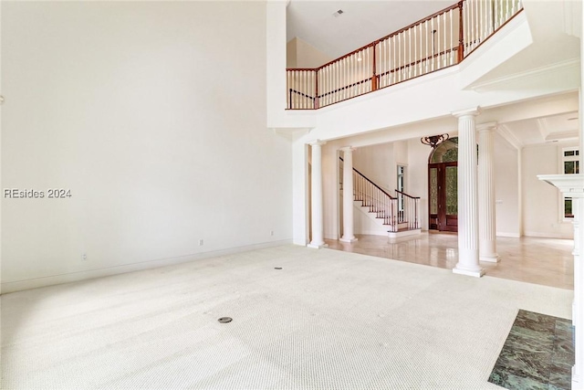 unfurnished living room featuring a towering ceiling, carpet, and ornate columns