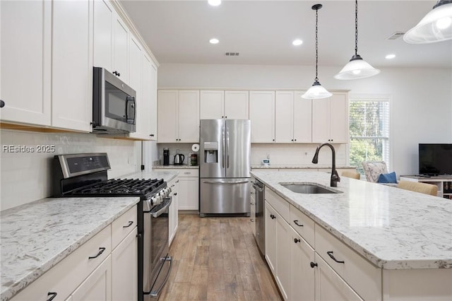 kitchen featuring sink, white cabinetry, appliances with stainless steel finishes, an island with sink, and pendant lighting