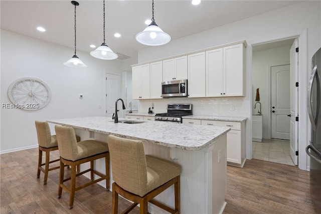 kitchen featuring sink, white cabinetry, decorative light fixtures, stainless steel appliances, and a kitchen island with sink