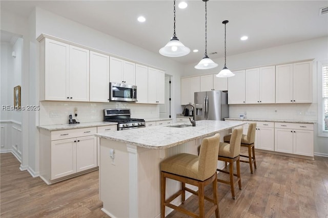 kitchen with white cabinetry, stainless steel appliances, sink, and a kitchen island with sink