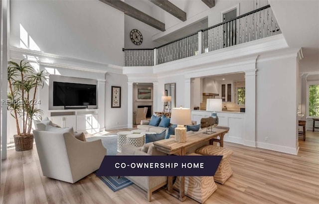 living room featuring beam ceiling, light hardwood / wood-style floors, decorative columns, and a high ceiling