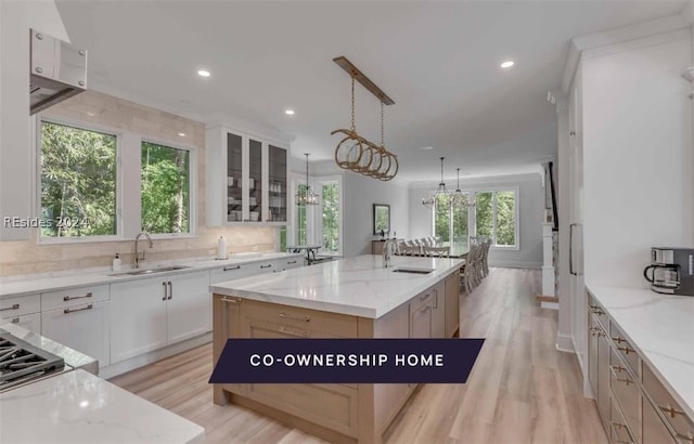 kitchen with decorative light fixtures, white cabinetry, light stone countertops, light wood-type flooring, and a spacious island