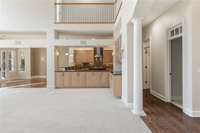 kitchen with tasteful backsplash, wall chimney exhaust hood, a high ceiling, and ornate columns