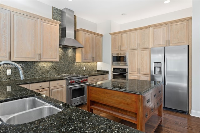 kitchen with wall chimney exhaust hood, sink, dark stone counters, stainless steel appliances, and backsplash