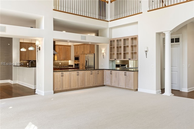 kitchen featuring a towering ceiling, decorative columns, decorative backsplash, light colored carpet, and stainless steel appliances