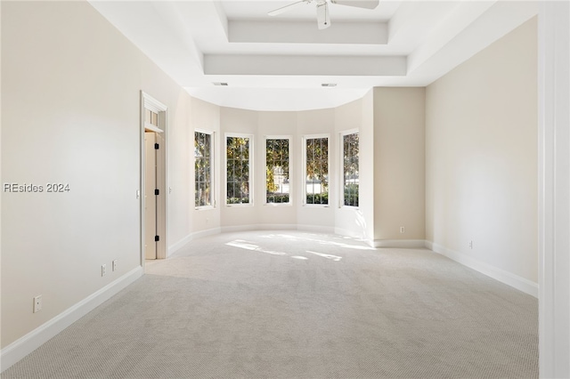 empty room featuring light colored carpet, ceiling fan, and a tray ceiling