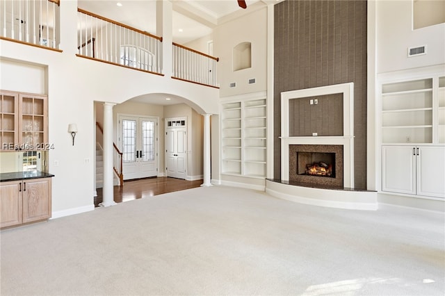 unfurnished living room with ornate columns, carpet, built in features, and a high ceiling