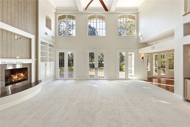 unfurnished living room featuring french doors, ornamental molding, carpet floors, beamed ceiling, and a towering ceiling