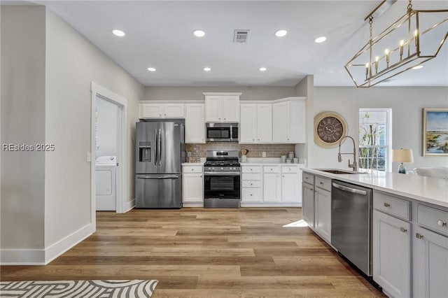 kitchen with white cabinetry, washer / dryer, sink, hanging light fixtures, and stainless steel appliances