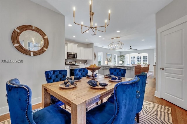 dining room with ceiling fan with notable chandelier and light wood-type flooring