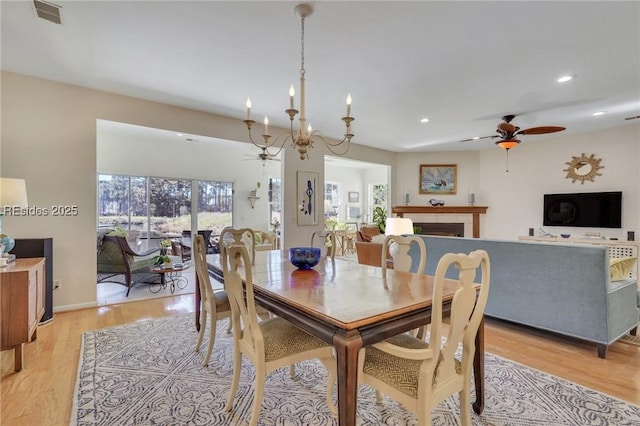 dining area featuring ceiling fan with notable chandelier, a fireplace, and light hardwood / wood-style flooring