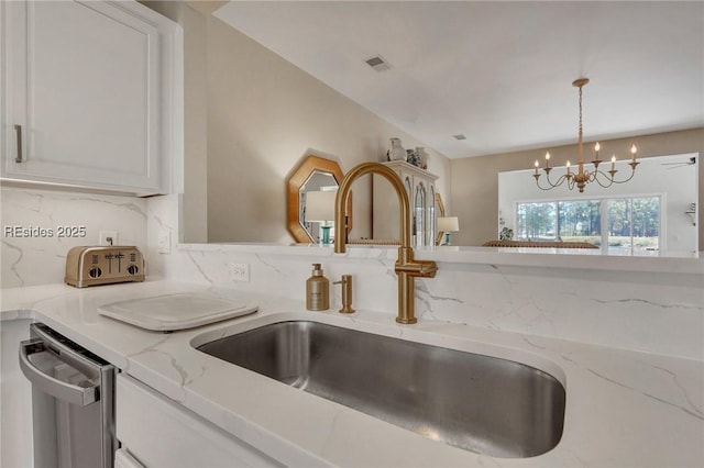 kitchen with sink, dishwasher, light stone counters, a notable chandelier, and decorative light fixtures